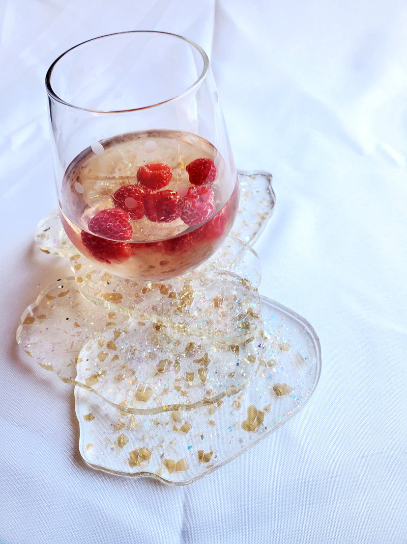Glass of wine with raspberries sitting on a pile of clear shattered glass resin coasters.